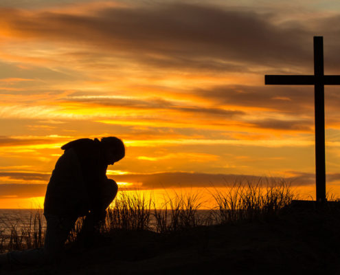 Man praying in front of cross at sunset